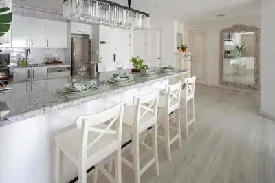 a white kitchen with a bar with white stools at Frank Porter - Fairmont Residence South in Dubai
