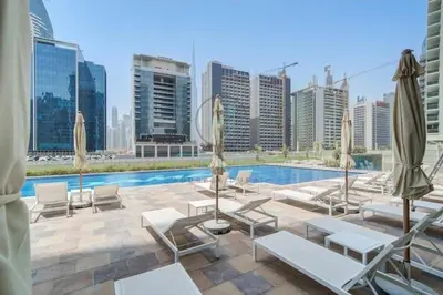 a pool with chairs and umbrellas on a building at Elegant 1BR with Sofa Bed Close to Metro in Dubai