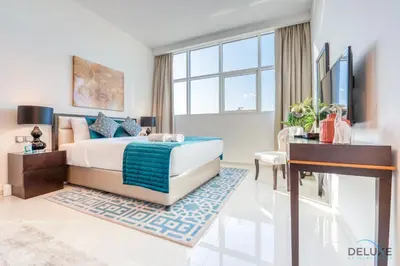 a bedroom with a bed and a desk and a television at Intimate Studio in Damac Ghalia Jumeirah Village Circle by Deluxe Holiday Homes in Dubai
