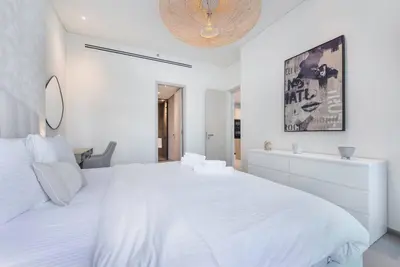 a white bedroom with a large white bed and a mirror at Modern flat with KING SIZE bed and HIGH SPEED Wifi in Dubai