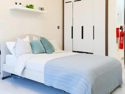 a white bedroom with a white bed with blue pillows at Elite LUX Holiday Homes - Modern Style Studio Superior Facilities in Arjan Dubai in Dubai