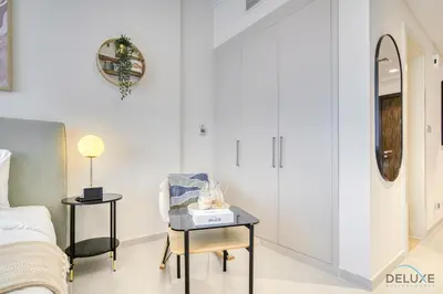 a bedroom with a bed and a table with a chair at Calm Studio at Carson C DAMAC Hills Dubailand by Deluxe Holiday Homes in Dubai