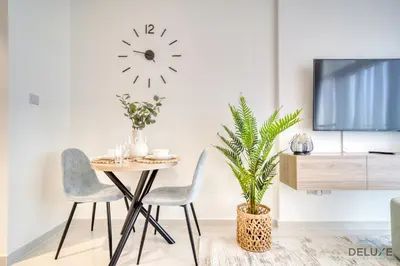 a dining room with a table and chairs and a clock on the wall at Calm Studio at Carson C DAMAC Hills Dubailand by Deluxe Holiday Homes in Dubai