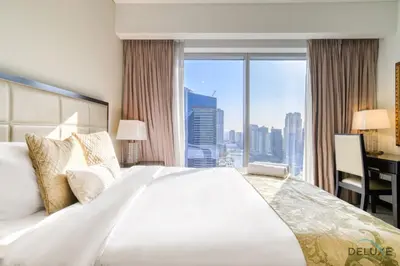 a bedroom with a large bed with a desk and a window at Overlooking Marina Canal Views from Living to Bedroom, The Address Residences, Dubai Marina by Deluxe Holiday Homes in Dubai