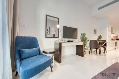 a living room with a blue chair and a television at Luxuriant Studio at Golf Promenade 2A DAMAC Hills by Deluxe Holiday Homes in Dubai