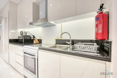 a white kitchen with a sink and a red fire extinguisher at Stunning Studio at Golf Promenade 2A Damac Hills by Deluxe Holiday Homes in Dubai