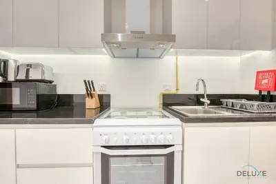 a white kitchen with a stove and a sink at Stunning Studio at Golf Promenade 2A Damac Hills by Deluxe Holiday Homes in Dubai