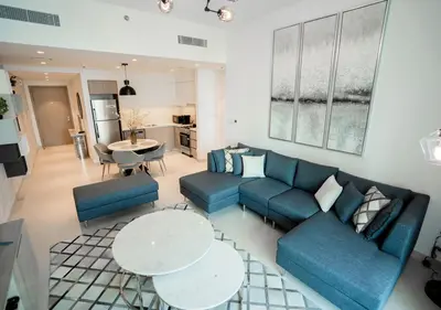 a living room with blue couches and tables and a kitchen at Nasma Luxury Stays - The Grand, Dubai Creek Harbour in Dubai
