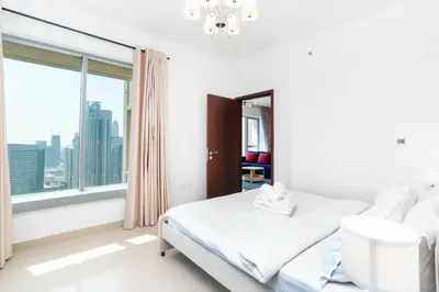 a white bedroom with a bed and a large window at Lux BnB I 29 Burj BLVD I Downtown Views in Dubai