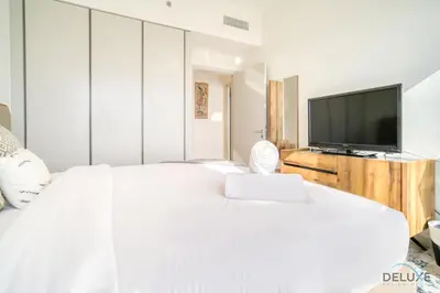 a white bedroom with a large bed and a flat screen tv at Splendid 2BR at Sunrise Bay Tower 1 Emaar Beachfront Dubai Marina by Deluxe Holiday Homes in Dubai