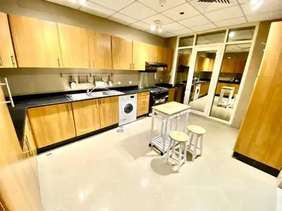 a kitchen with wooden cabinets and a table and stools at Marina Crown Tower Stays Hostel for Girls in Dubai