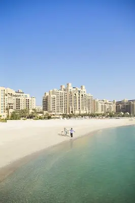 a group of people walking on a beach with tall buildings at Fairmont The Palm Residences I Access to Hotel Facilities in Dubai