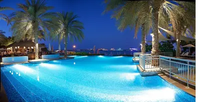 a large swimming pool with palm trees at night at Luxury Beachfront Palm Jumeirah I Free 5 Star Beach Resorts Access in Dubai
