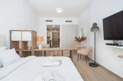 a white bedroom with a large bed and a table at Nice Studio in JVC - Pool & Gym in Dubai