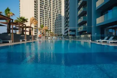 a large blue swimming pool with palm trees and buildings at Nice Studio in JVC - Pool & Gym in Dubai
