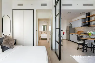 a bedroom with a white bed and a kitchen at Chic One Bedroom Suite with Cozy Interiors in Dubai