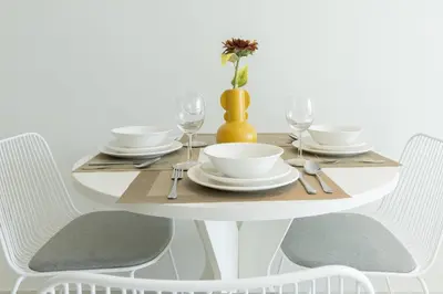 a white table with chairs and a white table with glasses at Tranquil 1BR apartment in Carson C, Damac Hills - Allsopp&Allsopp in Dubai