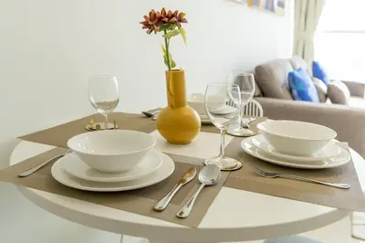 a table with plates and glasses and a vase at Tranquil 1BR apartment in Carson C, Damac Hills - Allsopp&Allsopp in Dubai