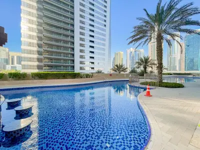 a swimming pool with palm trees and a tall building at Cosy 1 Bedroom Marina Apartment in Dubai