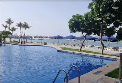 a swimming pool next to a beach with blue umbrellas at Elegant 2 BR Apartment with Beach Access in Dubai