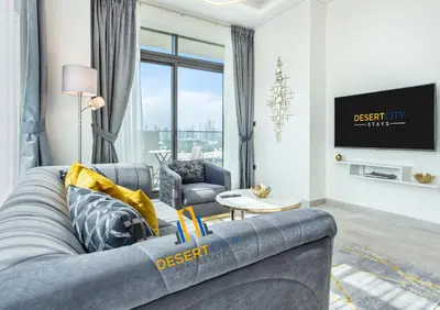 a living room with a gray couch and a tv at 2 Bed in Azzizi Farhad with Burj Khalifa view by Desert City Stays in Dubai