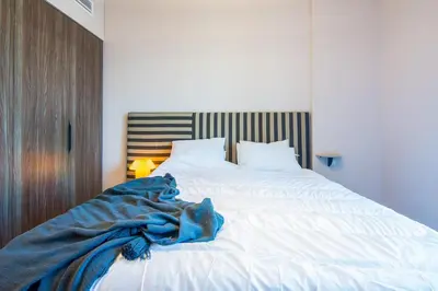 a large white bed with a blue blanket on it at Burj Al Arab View - 1BR in MJL Lamtara 1- Burj Al Arab View 703 in Dubai