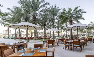 a restaurant with tables and umbrellas and palm trees at Ultra Luxe 5BR Al Bateen I Private Beach and Pool I JBR Full Sea View Beachfront in Dubai