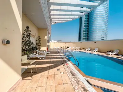 a hotel swimming pool with chairs and a tall building at Cosmos Living Elegant Studio Near Dubai Marina in Dubai