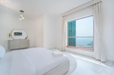 a white bedroom with a white bed and a window at JBR - Shams Suites - Sea & Marina View Walking Distance to The Beach by Gardenia in Dubai