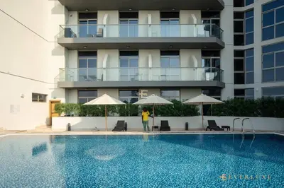 a person standing next to a swimming pool next to a building at Everluxe Azizi Montrell Lovely Studio in Dubai