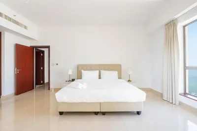 a white bedroom with a large bed and windows at Deluxe Retreat In JBR - Million Dollar View - Balcony in Dubai