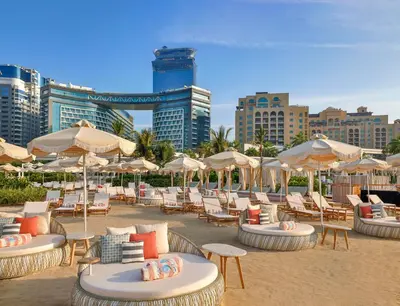 a beach with chairs and tables and umbrellas and buildings at NH Collection Dubai The Palm in Dubai