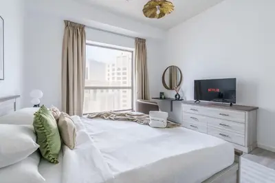 a white bedroom with a large bed and a television at GuestReady - Lux Aeterna in JBR in Dubai
