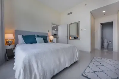 a white bedroom with a large bed and a bathroom at Bright and spacious apartment in DAMAC HILLS in Dubai