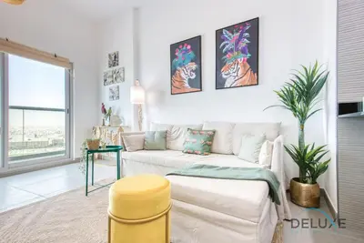 a living room with a white couch and a yellow stool at Vibrant 1BR in Bella Rose Al Barsha South by Deluxe Holiday Homes in Dubai