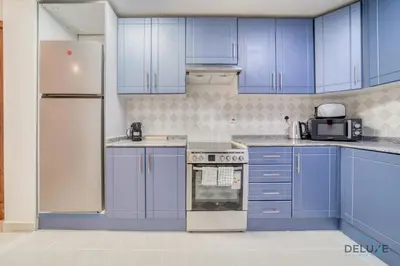 a kitchen with blue cabinets and a white refrigerator at Harmonious 1BR at Al Shera Tower JLT by Deluxe Holiday Homes in Dubai
