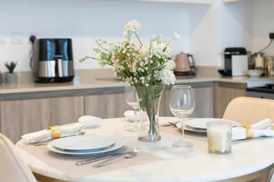 a table with plates and a vase of flowers on it at BNew Chic 1BR Apt Near Trump Golf w Pool and Gym in Dubai
