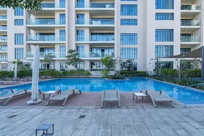 a swimming pool with chairs and a building at Vogue Emirates Hills, Vida The Hills Residence near Marina and JBR, One Bedroom Apartment with Balcony, Golf Club and City Skyline View, Access to all Amenities in Dubai