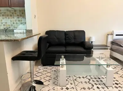 a living room with a black couch and a glass table at Studio - Steps from Downtown in Dubai