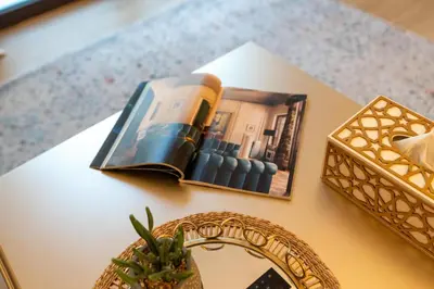 a book on a table with a mirror and a plant at Stylish 1BR Apartment in La Mer Dubai with Balcony and Partial Marina Views in Dubai