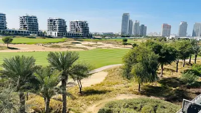 a view of a golf course with palm trees and buildings at Newly Furnished bright and cozy studio apartment - Damac Hills in Dubai