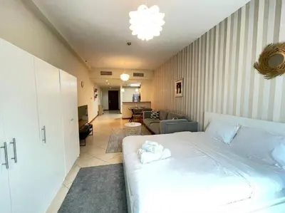 a bedroom with a large white bed and a living room at Amazing Largest Studio in Marina Next to Metro - Central Location in Dubai