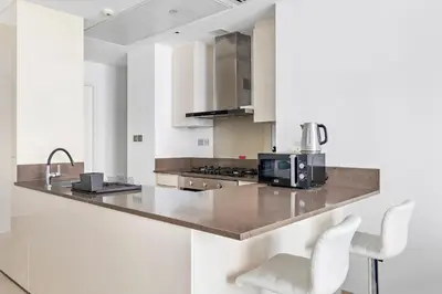 a kitchen with white cabinets and a counter with white chairs at StoneTree - Marina Gate 2 BR - Prime location in Dubai