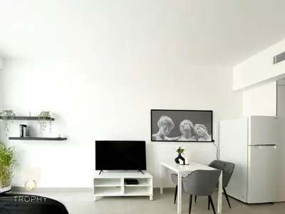 a white living room with a tv and a table at Stylish Studio Apartment in JVC with Contemporary in Dubai