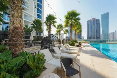 a pool at a hotel with white chairs and palm trees at ALiving Stylish Studio with Balcony I Partial Burj Khalifa View I DAMAC Maison Prive B-1315 in Dubai