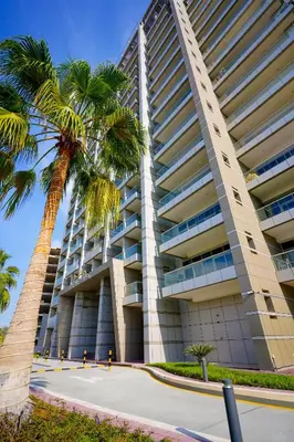 a tall building with a palm tree in front of it at Alashrafia Saray 2BR apartment in Sport City in Dubai