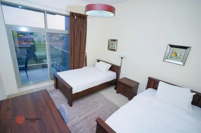 a room with two beds and a table and a window at Alashrafia Saray, Lovely 2 BR apartment in Sport city in Dubai