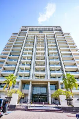 a tall white building with palm trees in front of it at Alasharafia Saray, Spacious 1BR apartment in Sport City in Dubai