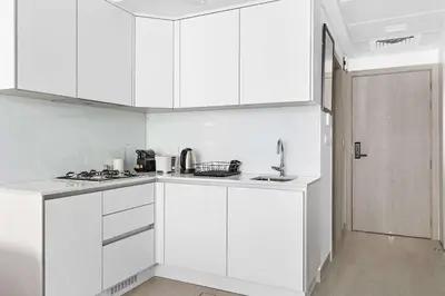 a white kitchen with white cabinets and a sink at Silkhaus cozy studio in JVC Luma21 in Dubai