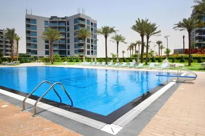 a large swimming pool with chairs and palm trees at Classic 1BR at MAG 510 Dubai South by Deluxe Holiday Homes in Dubai